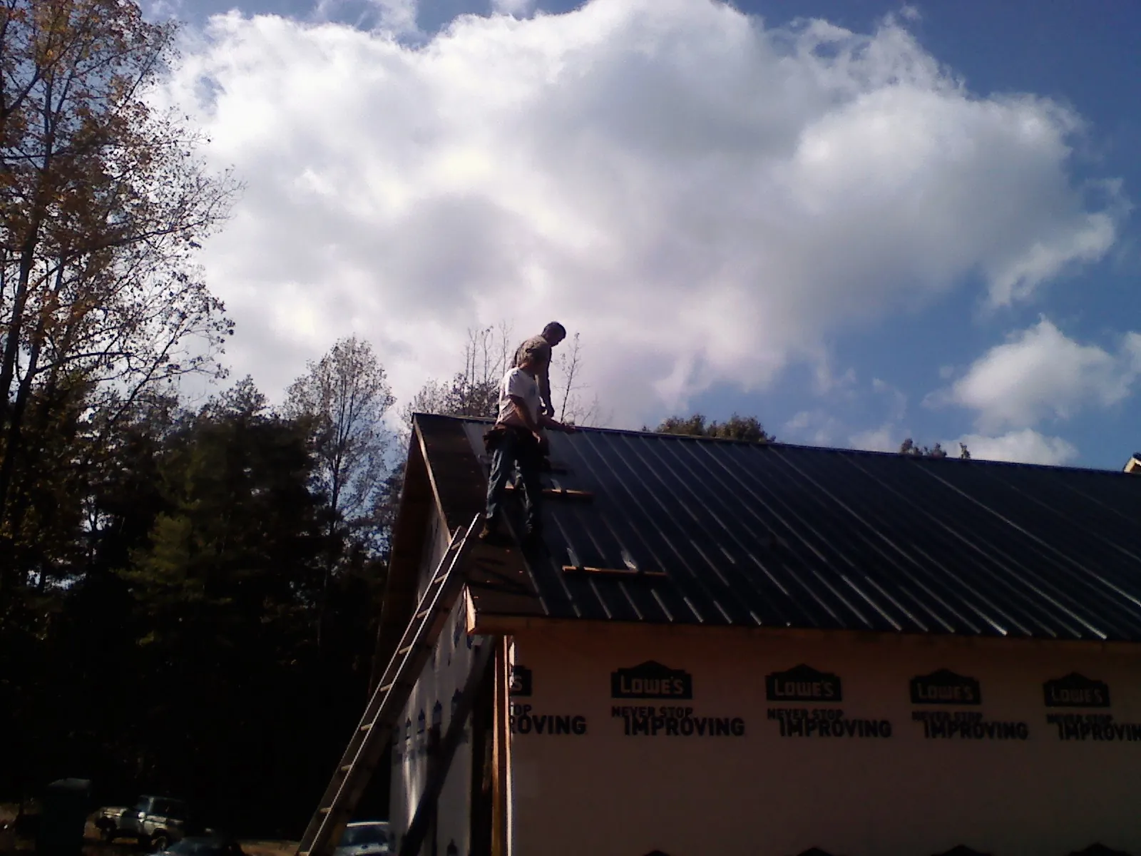 Roofer fastening dark metal panels high against a cloudy sky, from a Roof Inspection job in Valley